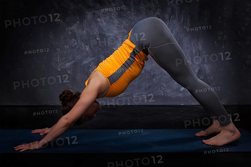 Beautiful sporty fit yogini woman practices yoga asana adhomukha svanasana, downward facing dog pose on dark background
