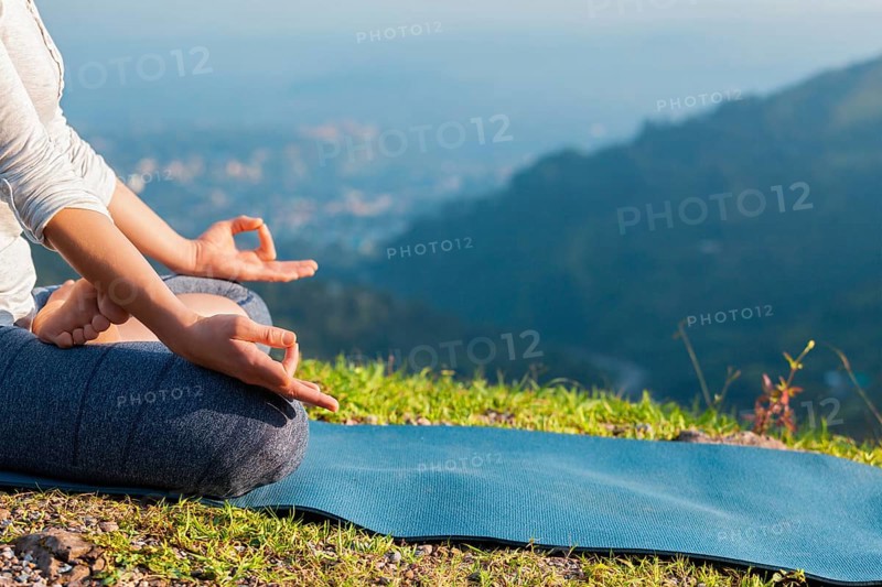 Meditation relaxation concept background, close up of woman in Padmasana yoga lotus pose with chin mudra outdoors with copyspace