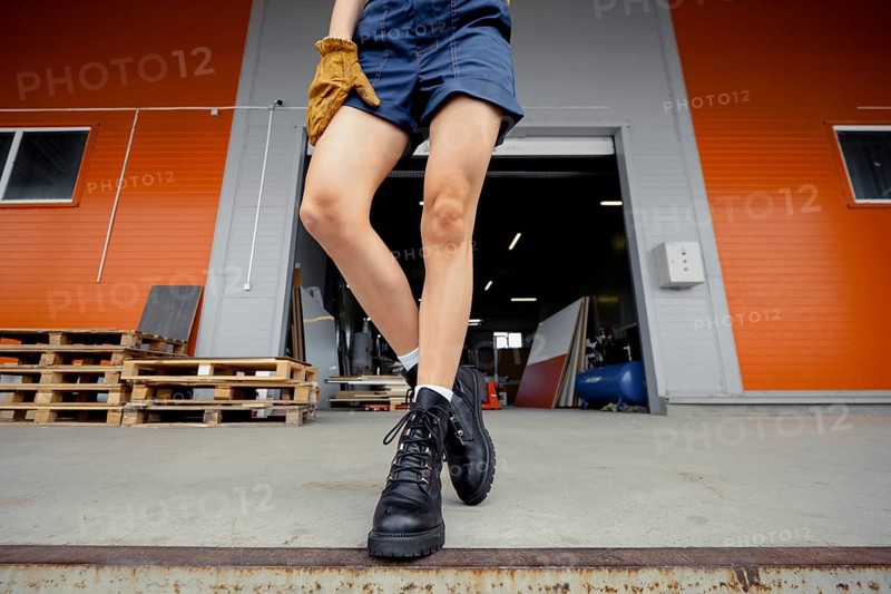 Low angle view at female legs in uniform and rough boots standing on ramp of warehouse