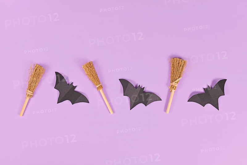 Halloween paper bats and witch brooms in a row on purple background