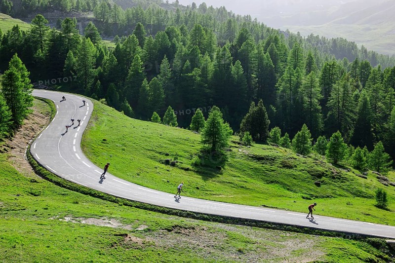Sporty young people skateboarding at high speed on switchbacks of alpine road pass road from pass Col de l Izoard Izoard pass downhill, Route des Grandes Alpes, French Alps, Département Hautes-Alpes, France, Europe