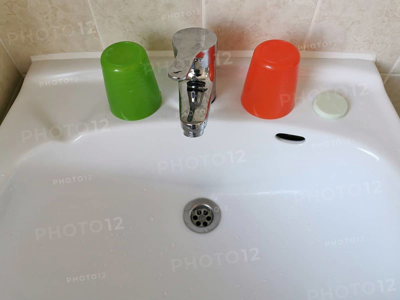 Washbasin with colourful plastic toothbrush cups and a bar of soap in a primitive hotel