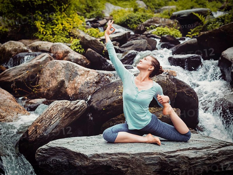 Vintage retro effect hipster style image of sporty fit woman doing yoga asana Eka pada rajakapotasana, one-legged king pigeon pose at tropical waterfall