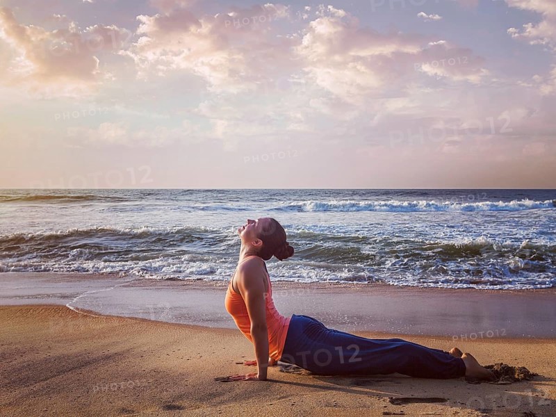 Yoga outdoors, woman doing Ashtanga Vinyasa yoga Surya Namaskar Sun Salutation asana Urdhva Mukha Svanasana, upward facing dog pose on sunset on beach. Vintage retro effect filtered hipster style image