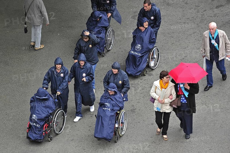 Disabled people in wheelchairs in the rain visiting Sanctuary of Our Lady of Lourdes, Pyrenees, France, Europe