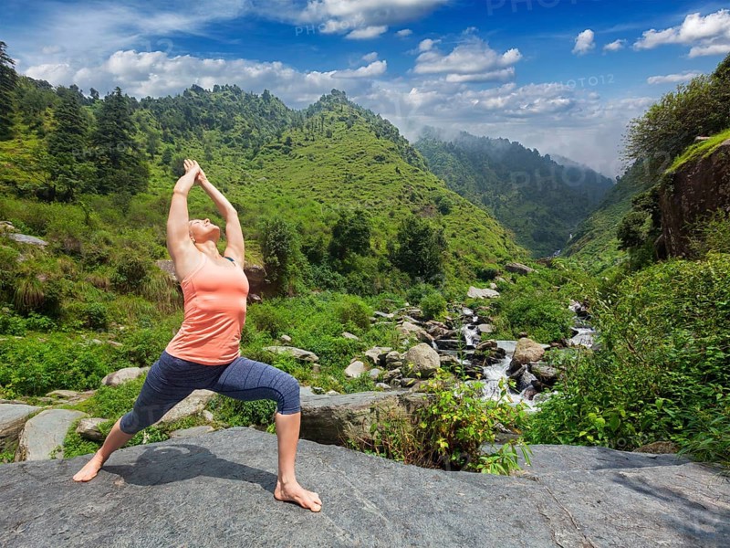 Yoga outdoors, sporty fit woman doing Ashtanga Vinyasa Yoga asana Virabhadrasana 1 Warrior pose posture at waterfall in HImalayas mountains