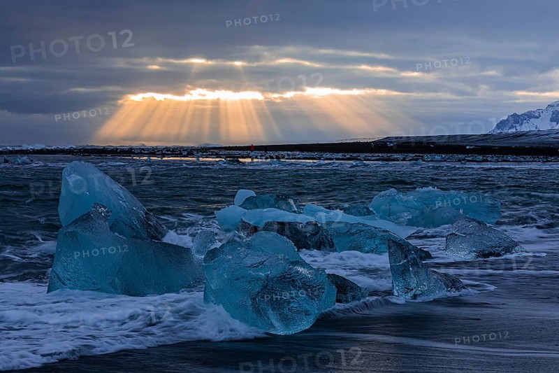 Waves breaking on icebergs on the black beach of Breidamerkursandur, sunset, near Jökullsarlon, Sudurland, Iceland, Europe