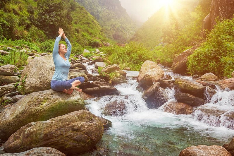 Woman doing yoga meditation asana Padmasana lotus pose outdoors at tropical waterfall