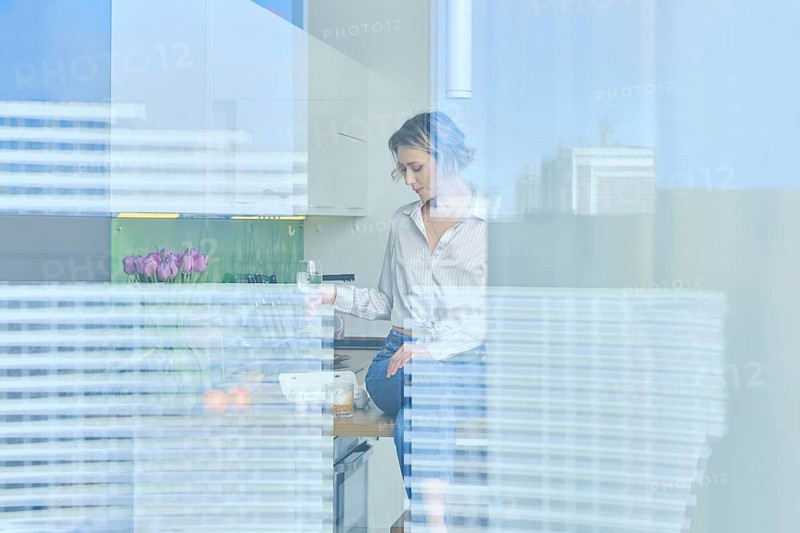 View through the window into the kitchen with beautiful woman inside sitting on teble top