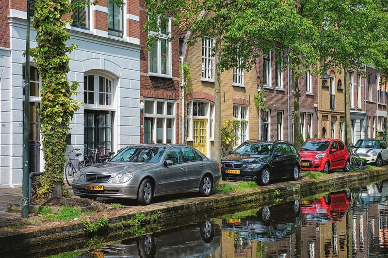 Delft, Netherlands, May 12, 2017: Cars and bicycles parked on canal embankment in street of Delft with reflection. Delft, Netherlands