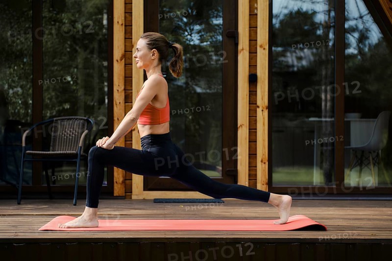 Woman warming up muscles on the wooden terrace of a country house, view in profile
