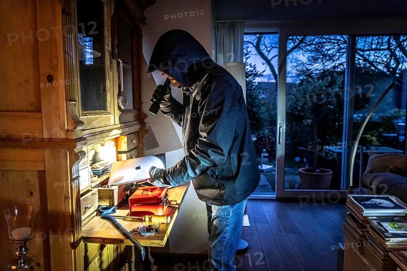 Symbolic image of a burglary, perpetrator has broken into a flat from the garden side and is looking for loot, computer, laptop, valuables, money, technology