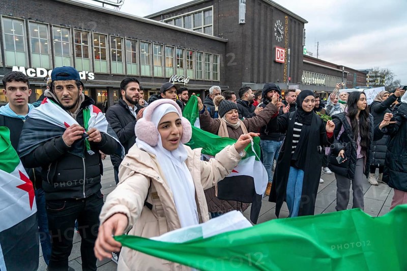 Syrian woman celebrate the end of the Assad regime after the change of power in Syria at a rally on the square in front of the main railway station in Duisburg, North Rhine-Westphalia, Germany, Europe