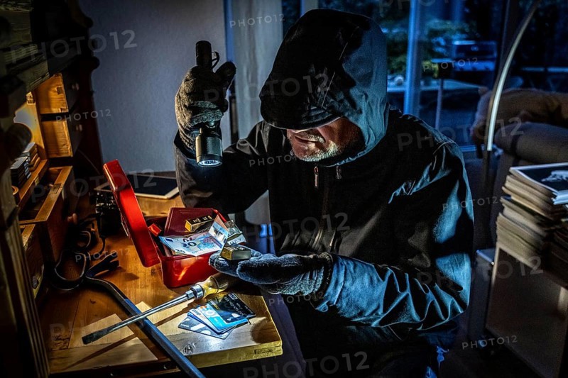 Symbolic image of a burglary, perpetrator has broken into a flat from the garden side and is looking for loot, breaks open a cash box, finds valuables, money