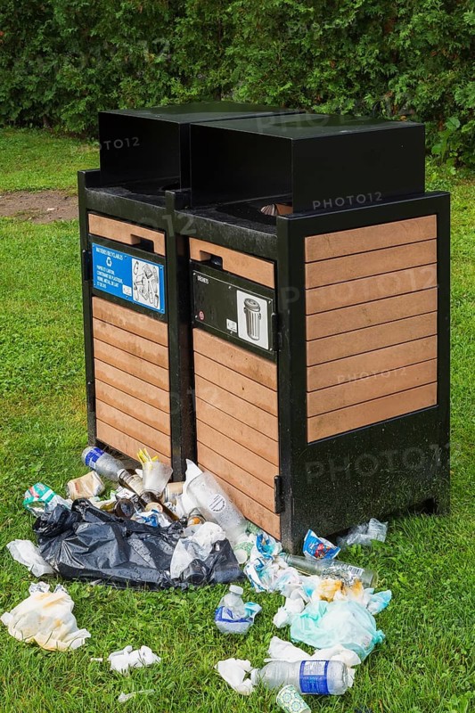 Black painted metal and natural wood garbage recycling bins with discarded thrash on green grass lawn in public garden park in summer, Quebec, Canada, North America