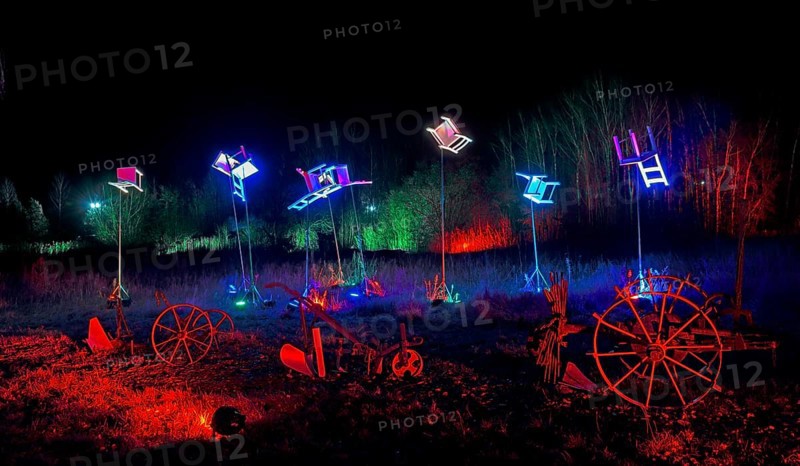 Artwork with colourful lights and chairs above wagon wheels at night, surrounded by trees, world of lights, illumination, Mill Museum, Gifhorn, Lower Saxony, Germany, Europe