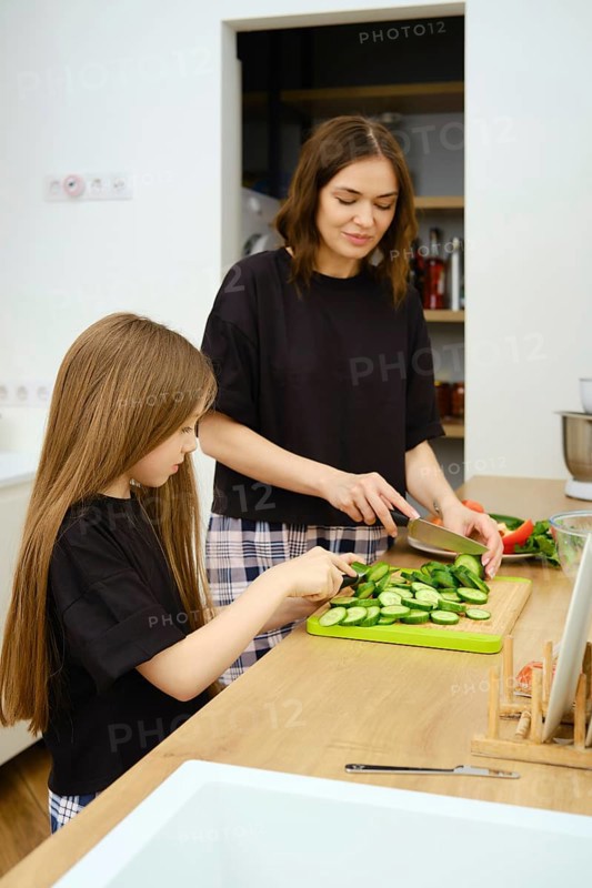 Mother and her daughter slicing organic cucumbers on wooden cutting board in the kitchen