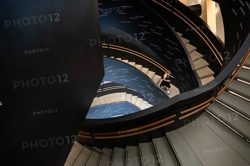 Woman on spiral staircase printed with Finnish words, Oodi Central Library and Cultural Centre, design by ALA Architects, Helsinki, Finland, Europe