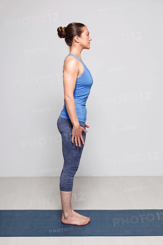 Woman doing Hatha Yoga asana Tadasana, Mountain pose with stretched hands on yoga mat in studio on grey bagckground