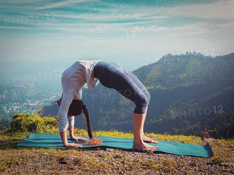 Yoga outdoors, young sporty fit woman doing Ashtanga Vinyasa Yoga asana Urdhva Dhanurasana, upward bow pose, in Himalayas mountains in the morning Himachal Pradesh, India. Vintage retro effect filtered hipster style image