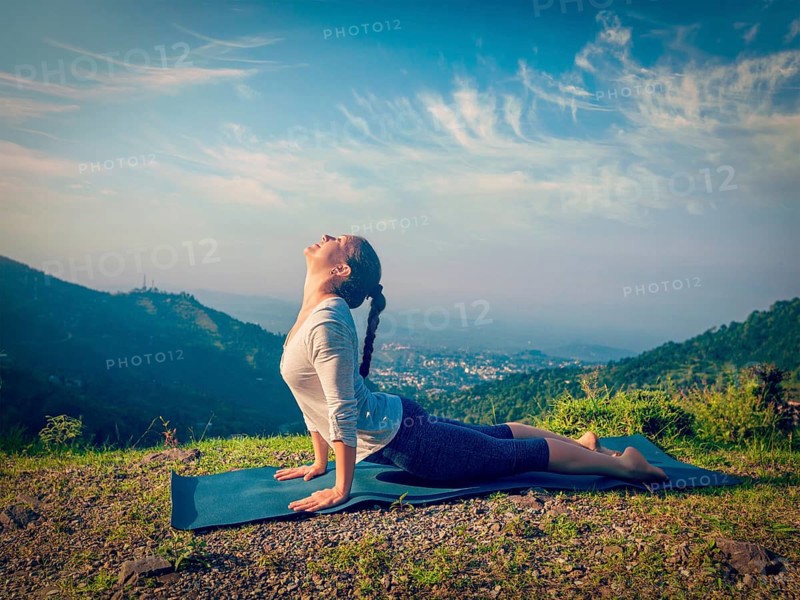 Yoga outdoors, woman practices Ashtanga Vinyasa yoga Surya Namaskar Sun Salutation asana Urdhva Mukha Svanasana, upward facing dog pose in mountains in the morning. Vintage retro effect filtered hipster style image