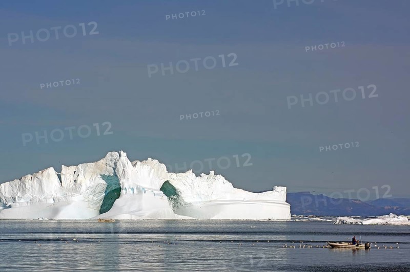 Small fishing boat surrounded by seabirds in front of iceberg with large ice cave, Ilulissat, Disko Bay, Denmark, Greenland, North America