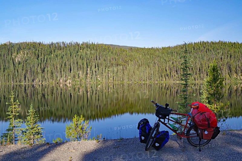 Bicycle standing by a crystal clear lake on an empty road, evening light, Stewart Cassiar Highway, British Columbia, Canada, North America