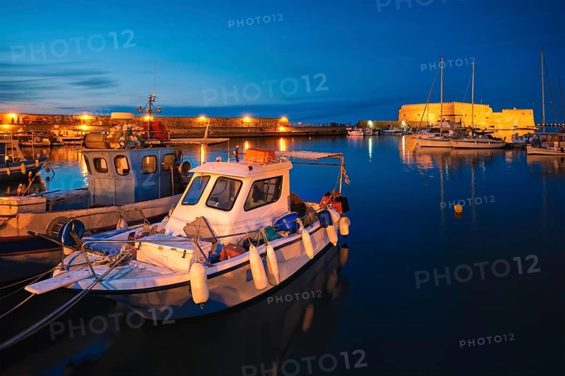 Venetian Fort castle in Heraklion and moored Greek fishing boats in port, Crete Island, Greece in twilight