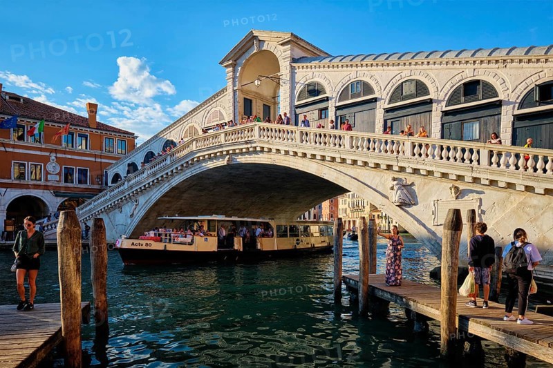 VENICE, ITALY, JUNE 27, 2018: Rialto bridge with vaporetto passing under on Grand Canal on sunset, Venice, Italy, Europe