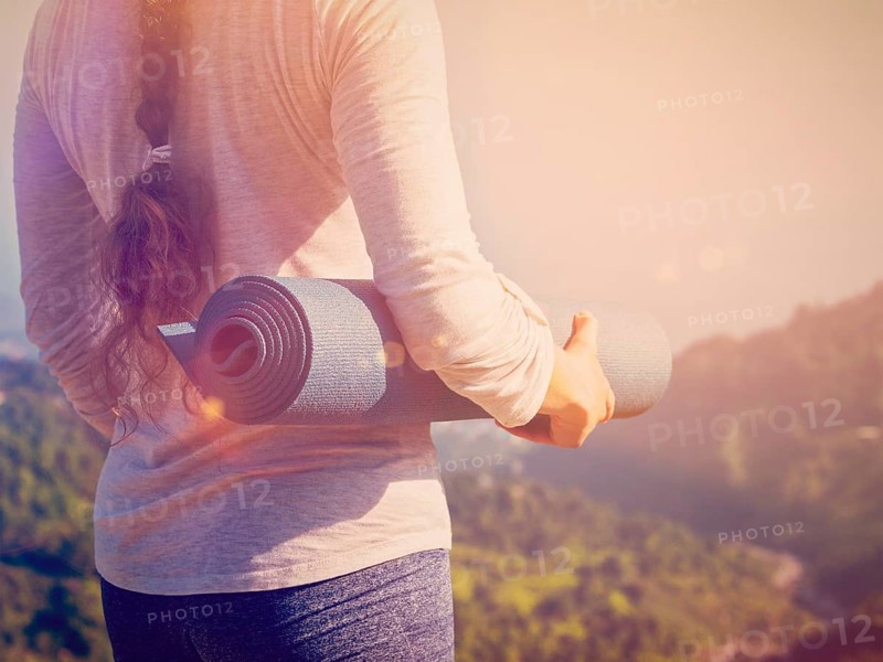 Woman standing with yoga mat outdoors in mountains close up with copyspace. With light leak and lens flare. Vintage retro effect filtered hipster style image