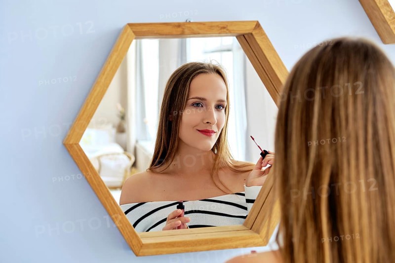 Pretty lady applying lipstick looking in the mirror