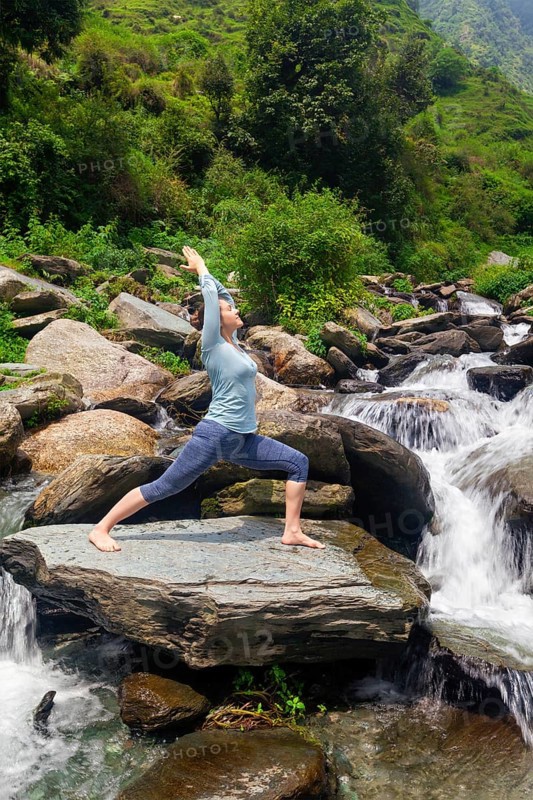 Yoga outdoors, sporty fit woman doing Ashtanga Vinyasa Yoga asana Virabhadrasana 1 Warrior pose posture at waterfall in HImalayas mountains