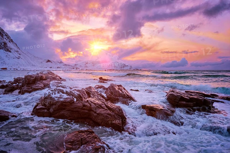Waves of Norwegian sea on rocky coast in fjord on sunset with sun. Skagsanden beach, Lofoten islands, Norway, Europe