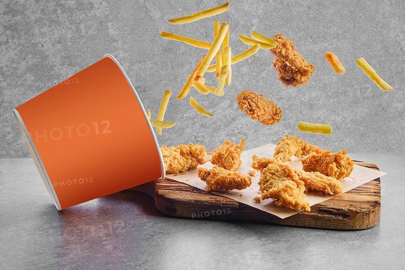 Deep fried chicken wings and nuggets in breading scattered from basket on parchment paper
