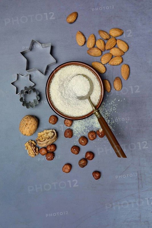 Grated coconut in a bowl and spoon, various nuts and cookie cutters