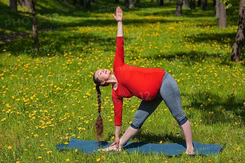 Pregnancy yoga exercise, pregnant woman doing asana Utthita trikonasana outdoors on grass in summer