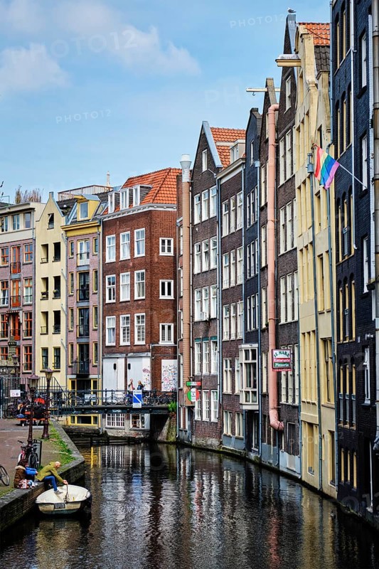 AMSTERDAM, NETHERLANDS, MAY 7, 2017: Amsterdam canal with boat, bridge and old houses with Gay Pride Rainbow flag. In 2001 the Netherlands became the 1st country to establish same-sex marriage by law