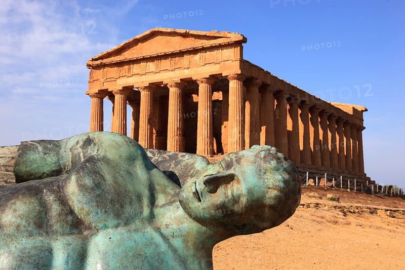 In the Parco Valle dei Templi di Agrigento, Unesco World Heritage Site, remains of the ancient city of Akragas in the Valley of the Temples of Agrigento, the Temple of Concordia with the sculpture of the crashed Icarus by artist Igor Mitorgi, installed in 2012, Sicily, Italy, Europe