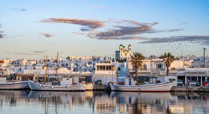 View of Naoussa, Fishing boats in the harbour at sunset, reflected in the sea, White Cycladic houses and church Agios Faneromeni, Naoussa, Paros, Cyclades, Greece, Europe