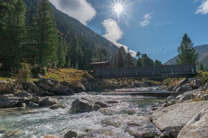 Wooden bridge over Zamser Bach in the valley Zamser Grund, Schlegeis, hiking trail, coniferous forest, rocks, backlight, blue sky, Zillertal Alps, Tyrol, Austria, Europe