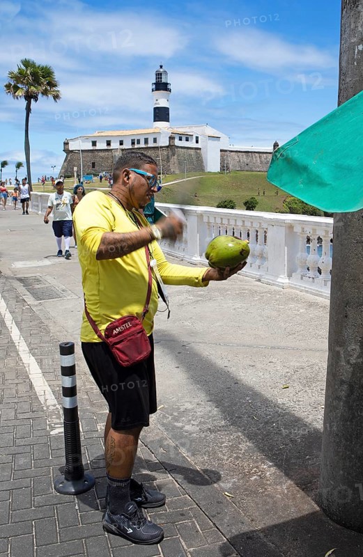 Brazilian man opening a coconut, Faro da Barra lighthouse in the back, Salvador, State of Bahia, Brazil, South America