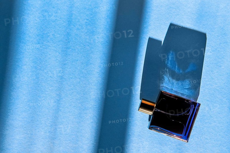 Bottle of perfume for men on blue background under sun light from the window