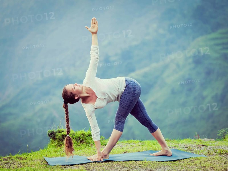 Vintage retro effect hipster style image of woman doing Ashtanga Vinyasa yoga asana Parivrtta trikonasana, revolved triangle pose outdoors