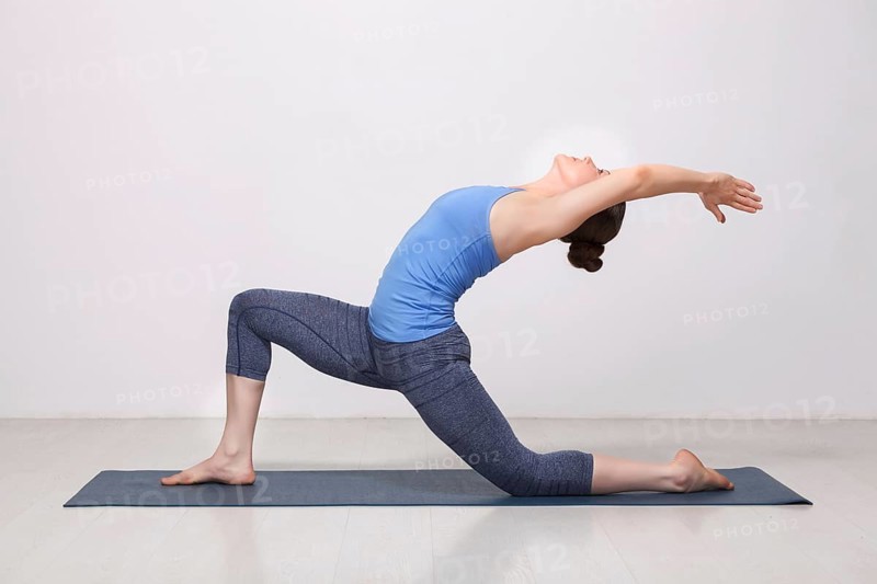 Beautiful sporty fit yogini woman practices yoga asana Anjaneyasana, low crescent lunge pose in surya namaskar in studio
