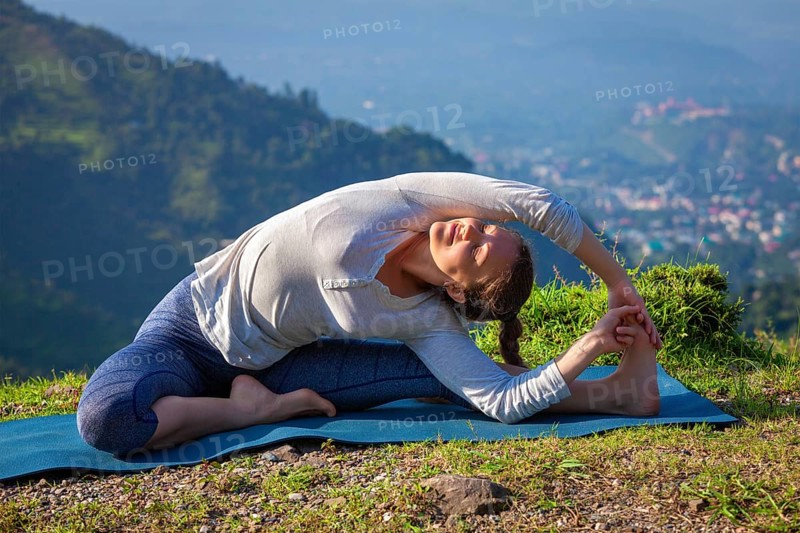 Yoga outdoors, young sporty fit woman doing Hatha Yoga asana parivrtta janu sirsasana, Revolved Head-to-Knee Pose, in mountains in the morning