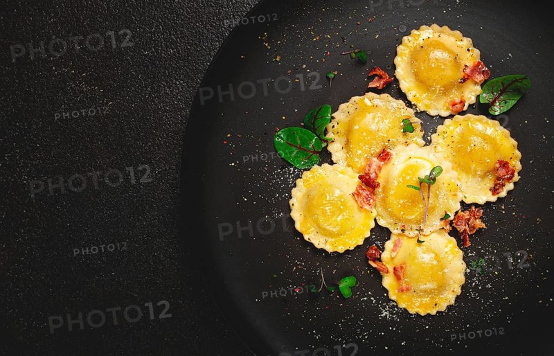 Fresh ravioli, with butter, spices and herbs, fried bacon, on a black plate, top view, dark background, no people