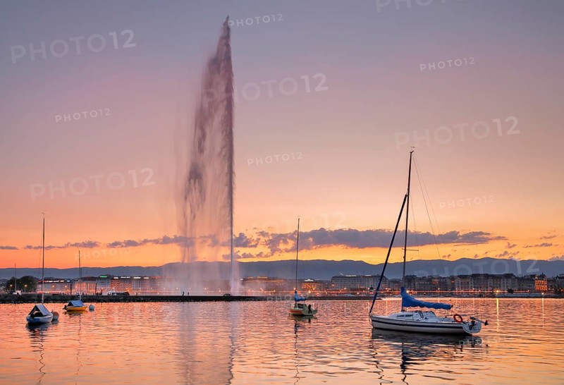 The Jet d'eau at dusk is the landmark in the Lake Geneva basin, with sailboats in the foreground and the lake promenade lit up at night in the background, Canton Geneva, Switzerland, Europe