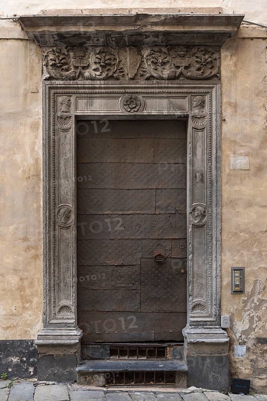 Historic entrance door with decorative floral reliefs on the frame in the historic city centre, Genoa, Italy, Europe