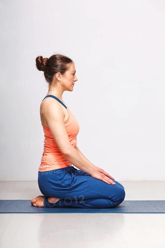 Woman in Hatha yoga asana Vajrasana, vajra pose or diamond pose on yoga mat on yoga mat in studio on grey bagckground
