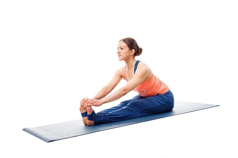 Woman doing Ashtanga Vinyasa Yoga asana Paschimottanasana, seated forward bend pose beginner variation isolated on white background